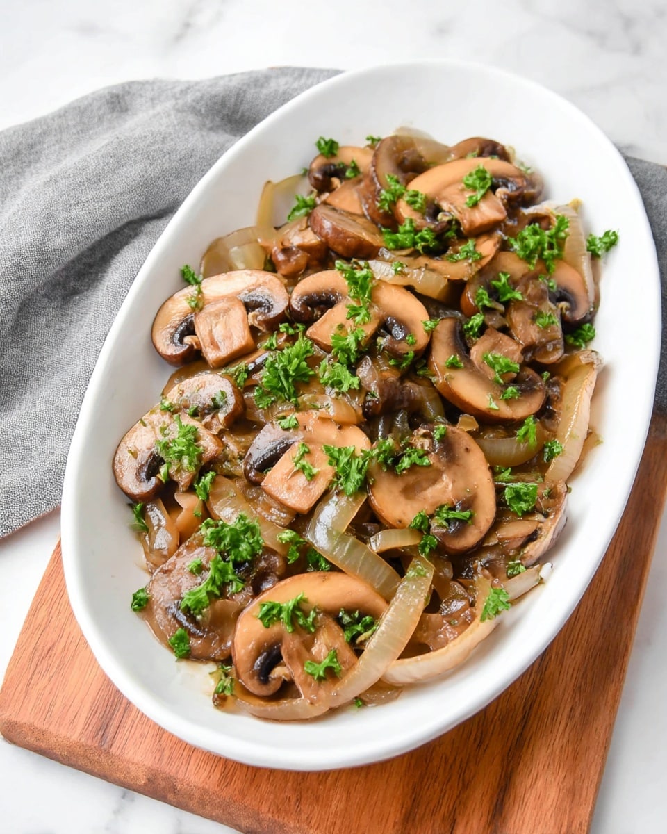 The image shows a close-up of cooked sliced mushrooms and onions in a black speckled pan. The mushrooms are brown with some caramelized edges, mixed evenly with translucent, soft onion slices. Bright green chopped herbs are scattered over the top, adding a fresh contrast. The dish appears juicy with a glossy texture from the cooking juices. The pan sits on a soft gray fabric, creating a cozy, home-cooked feel. photo taken with an iphone --ar 4:5 --v 7