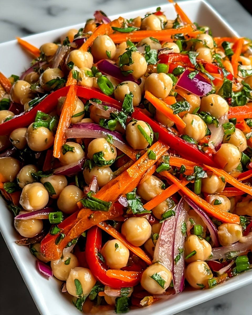 A close-up view of a colorful chickpea salad in a white square dish placed on a white marbled surface. The salad has a base layer of light beige round chickpeas, mixed with thin strips of bright orange carrots and red bell peppers. Among these are small pieces of purple onion and scattered chopped green herbs, adding vibrant green spots throughout. The textures range from soft chickpeas to crunchy vegetables, all glistening slightly with a dressing that gives a fresh and appetizing look. photo taken with an iphone --ar 4:5 --v 7