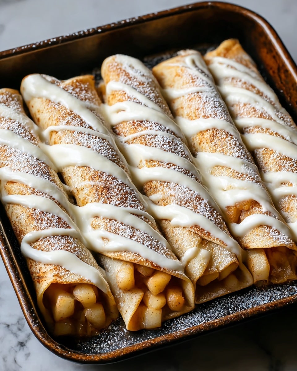 The image shows a close-up of two rolled crepes placed side by side, each filled with small pieces of cooked apples that are light yellow with a soft texture. The crepes have a light golden-brown surface with spots of deeper brown from cooking. On top of the crepes, a thick white icing is drizzled in even vertical lines, creating a smooth contrast against the golden crepes and light apple pieces. The overall focus is sharp on the front crepe with a blurred background, all set against a white marbled texture. photo taken with an iphone --ar 4:5 --v 7