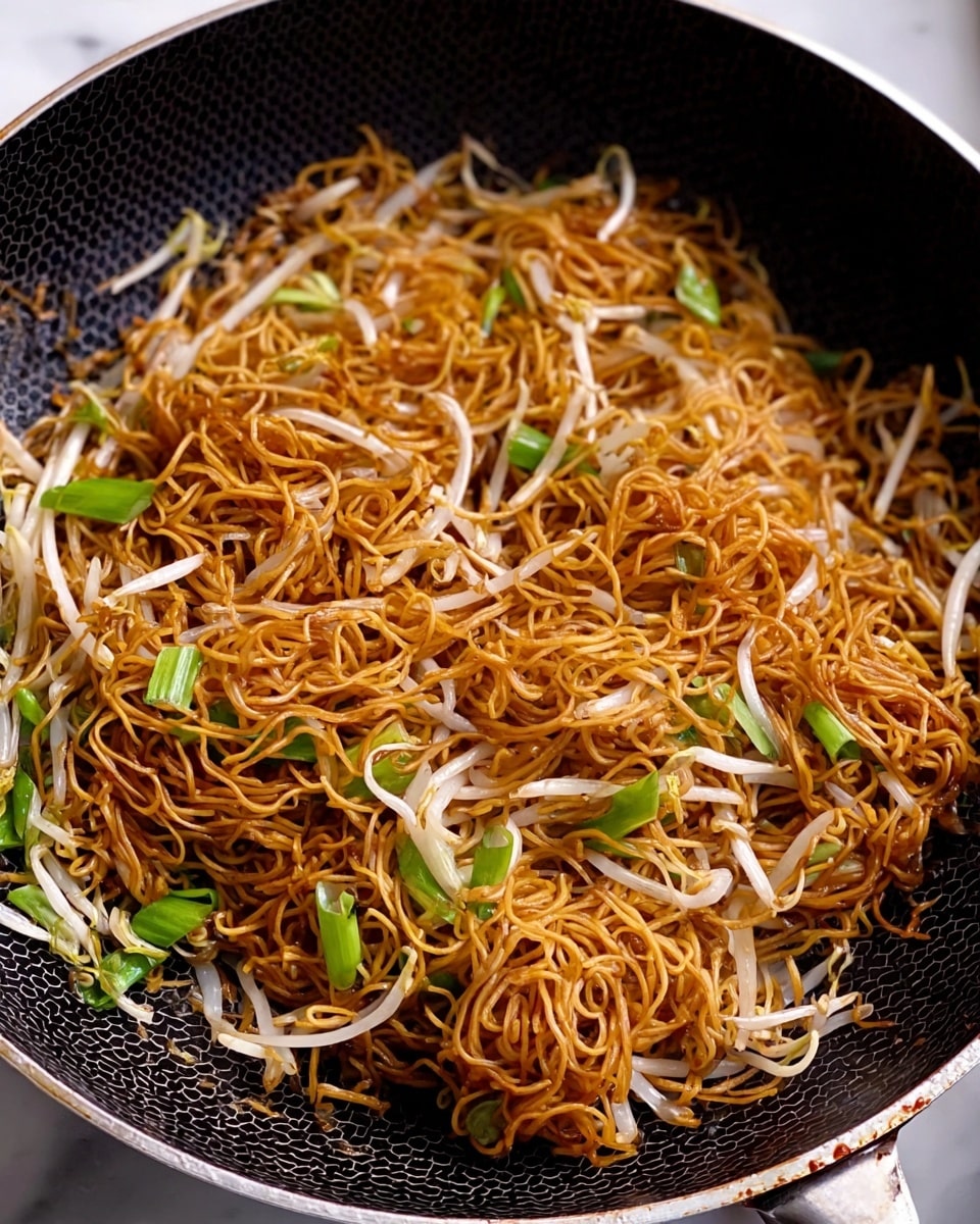 A white bowl filled with stir-fried noodles in a dark golden brown color, mixed with white bean sprouts and green leafy vegetables. Some noodles are being lifted by a woman's hand holding light wooden chopsticks, showing the texture and slight shine of the noodles. Another white bowl of the same noodle dish is visible in the background on a white marbled surface, with a green plant in a white rectangular pot beside it. A light pink and white checkered cloth is partially visible at the front. photo taken with an iphone --ar 4:5 --v 7