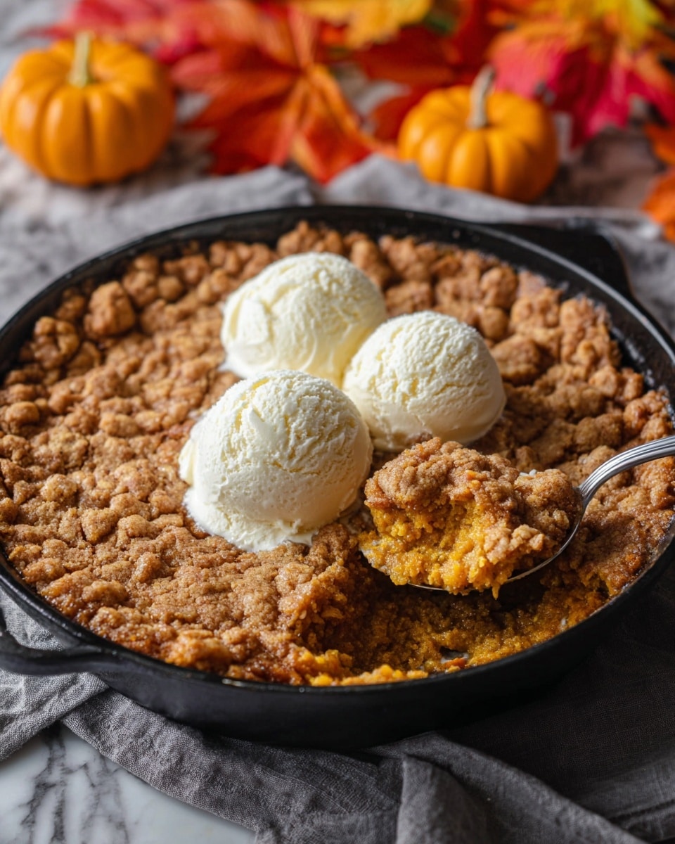 A black cast iron skillet filled with a warm, crumbly pumpkin dessert with a golden-brown textured top layer that looks crunchy. There are three smooth, round scoops of creamy vanilla ice cream placed in the center, slightly melting on the dessert. A spoon is scooping out a portion of the soft, moist pumpkin filling underneath the crispy topping, showing a rich orange color with a soft crumbly texture. The skillet sits on a gray cloth over a white marbled surface, and colorful autumn leaves and small pumpkins are blurred in the background, adding a cozy fall feel. photo taken with an iphone --ar 4:5 --v 7