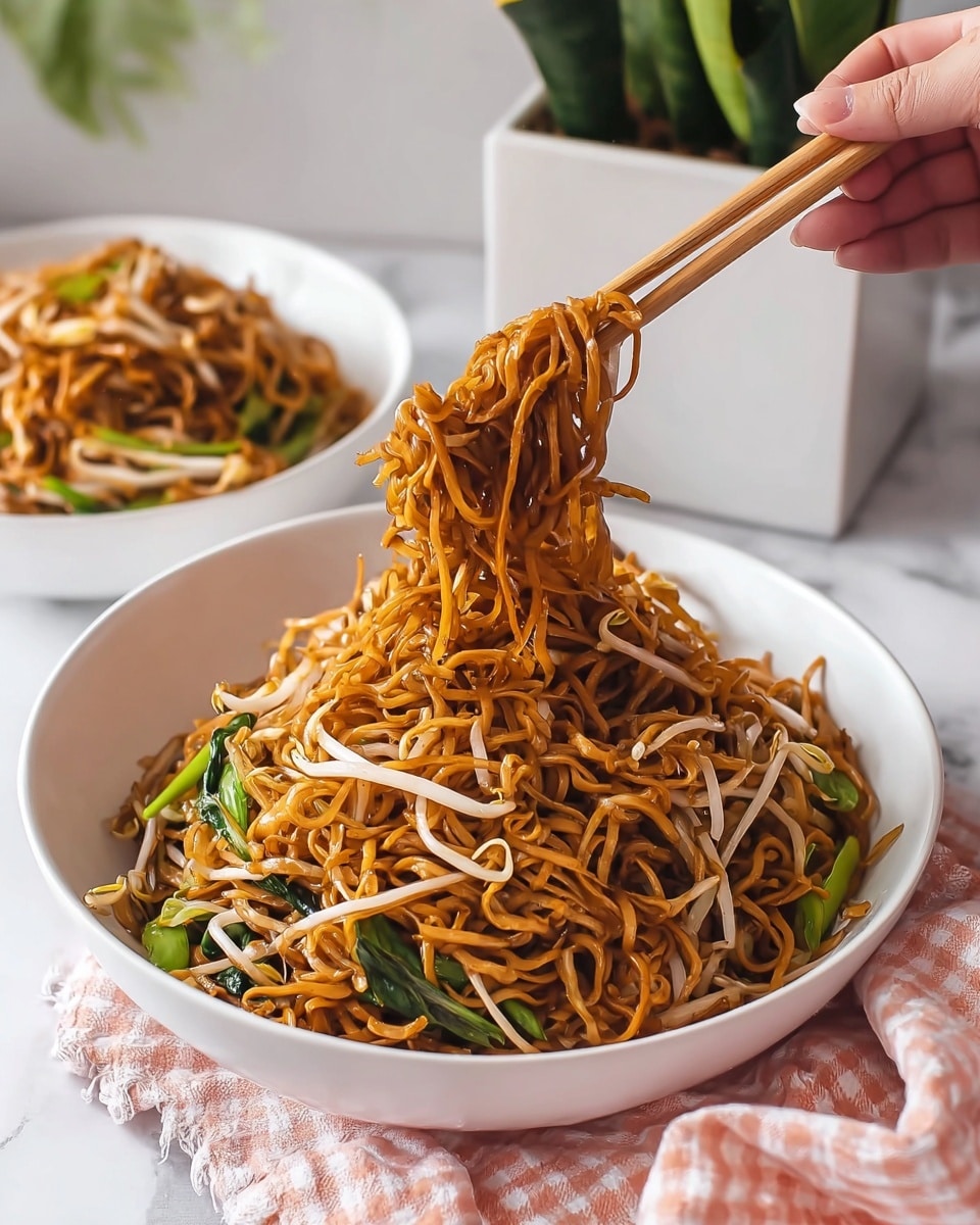 A close-up view of a pan filled with thin golden-brown fried noodles tangled loosely and mixed with light translucent white bean sprouts and a few vibrant green chopped scallions scattered evenly throughout. The noodles have a slightly oily and glossy texture, with some sections showing a crispier brown shade. The pan has a black hexagonal patterned non-stick surface with a silver edge visible around it, and the scene is set against a white marbled texture. Photo taken with an iphone --ar 4:5 --v 7