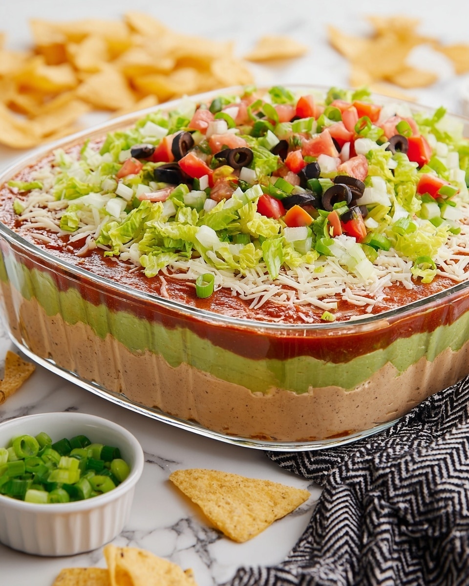 A clear glass dish holds a seven-layer dip with distinct layers visible from the side: the bottom layer is light brown refried beans, followed by a smooth green guacamole layer, then a thick beige creamy layer, a bright red salsa layer, a thin layer of shredded white cheese, and on top a colorful mix of chopped green lettuce, green onions, diced red tomatoes, and sliced black olives. The dish sits on a white marbled surface with white tortilla chips scattered around and a small white bowl with chopped green onions nearby. A black and white zigzag cloth is partially visible beside the dish. Photo taken with an iphone --ar 4:5 --v 7