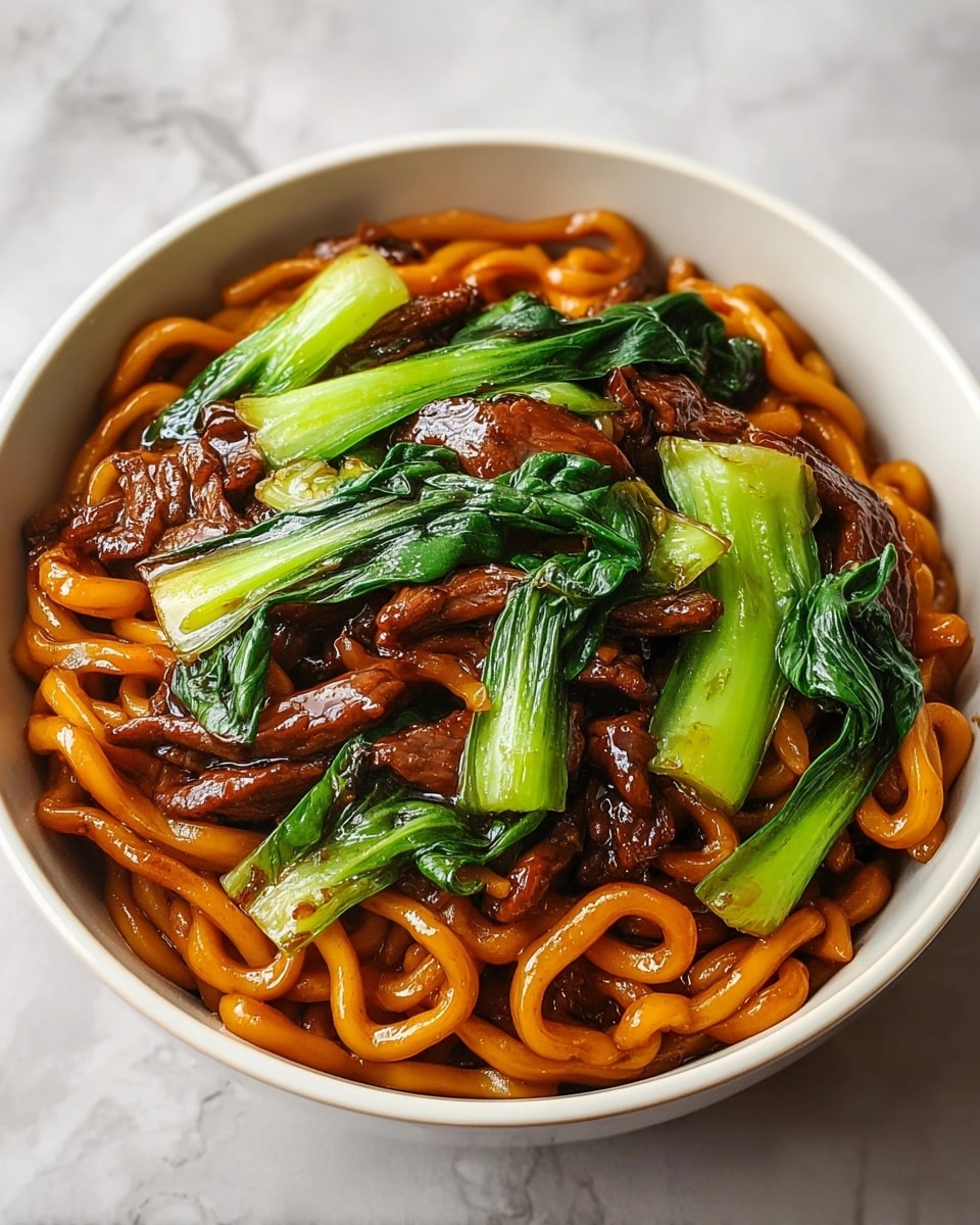 A white bowl contains a colorful dish with three main layers. The bottom layer is a bed of thick, shiny orange-brown noodles, twisted and glossy from sauce. Scattered through the noodles is the second layer, made of dark brown, tender-looking meat strips coated in sauce. On top, the third layer features bright green bok choy leaves and stems, fresh and slightly crisp, adding a pop of color and texture. The bowl rests on a surface with a white marbled texture. photo taken with an iphone --ar 4:5 --v 7