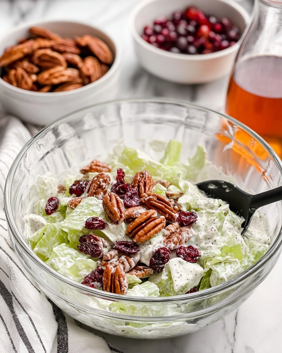 A clear glass bowl holds a fresh salad made of three main layers: the base layer consists of pale green celery pieces coated in creamy white dressing with visible black pepper specks, the middle layer is dotted with dark red dried cranberries, and the top layer features medium brown pecan halves scattered evenly. A black spoon rests inside the bowl, ready to mix the salad. In the background, there's a white bowl with more pecans and another white bowl filled with cranberries, set on a white marbled surface next to a glass container of amber liquid. A white cloth with black stripes is partly visible on the side. photo taken with an iphone --ar 4:5 --v 7