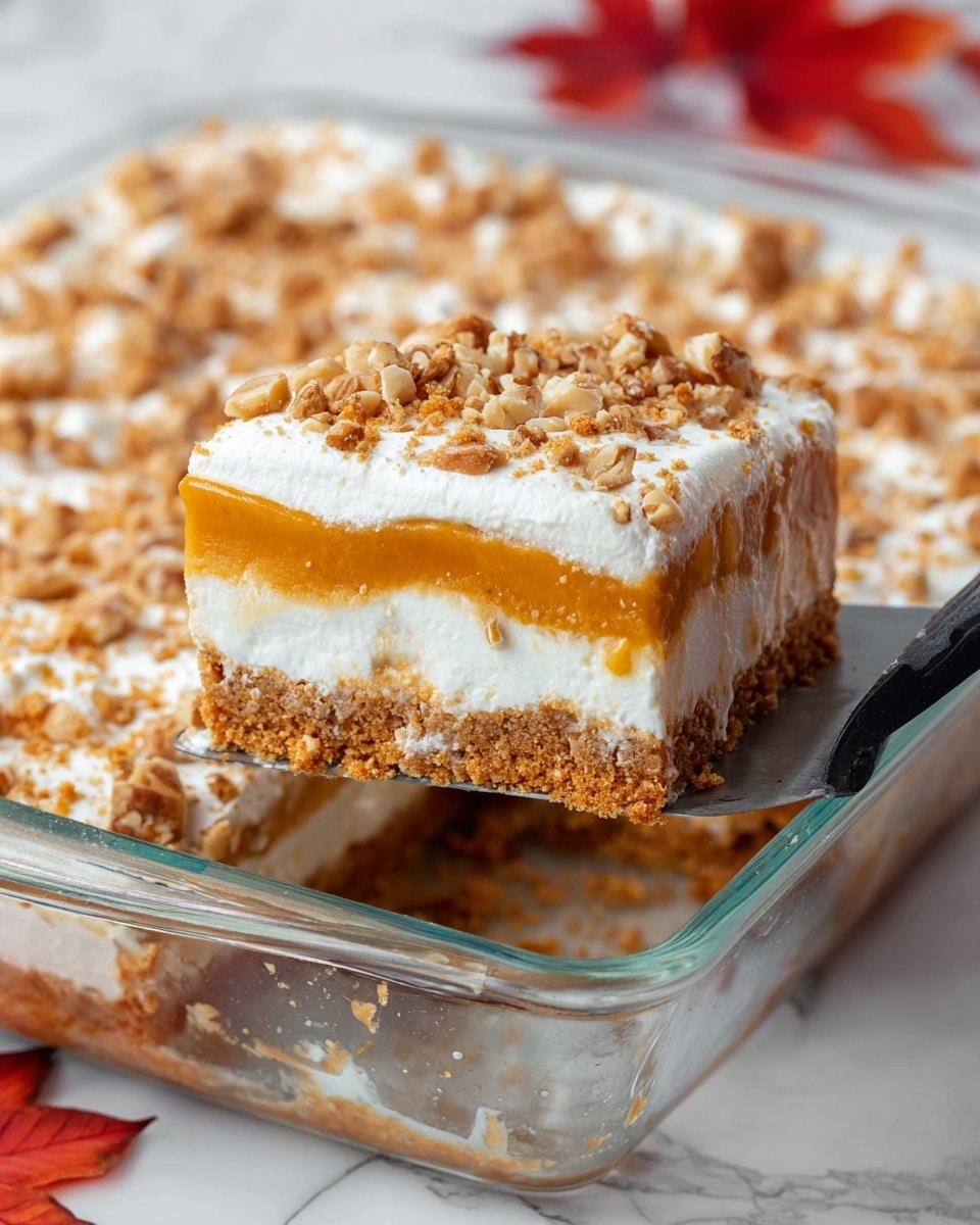 A close-up of a layered dessert in a clear glass rectangular dish resting on a white marbled surface, featuring four layers: a bottom layer of dense light brown crumb crust, a thick creamy white layer above it, topped with a smooth, shiny orange layer, and finished with a thick white whipped topping sprinkled with crushed nuts and crumbs. A metal spatula with a black handle is lifting a square piece from the dish, showing the distinct layers and creamy texture. Red autumn leaves are slightly visible in the background. Photo taken with an iphone --ar 4:5 --v 7