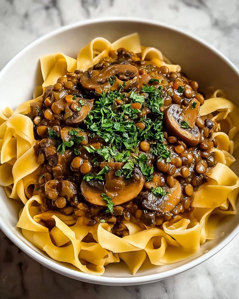 A white bowl filled with wide, flat cooked pasta ribbons at the bottom, soft and creamy yellow in color with a slightly glossy texture. On top is a rich brown sauce mixed with cooked lentils and sliced mushrooms, giving a chunky and hearty look with the mushrooms showing light and dark brown tones. The dish is finished with a sprinkle of fresh green chopped herbs on top, adding a pop of color against the warm, earthy sauce. The bowl sits on a white marbled texture surface. photo taken with an iphone --ar 4:5 --v 7