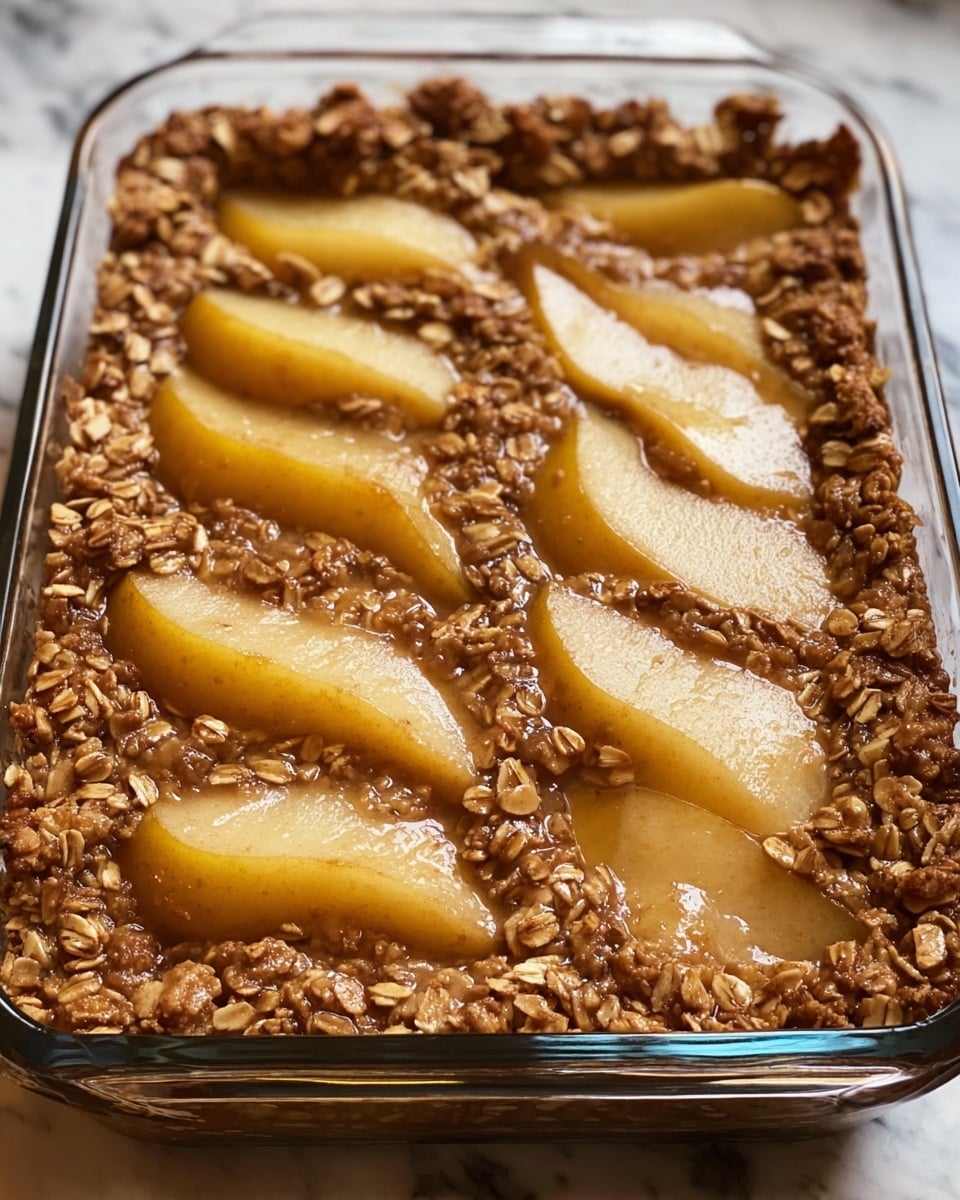 A clear glass baking dish filled with a warm, baked mixture of oats and soft, sliced pears. There is one layer visible, which is a thick, brown oat base with a sticky texture, dotted with whole oats. On top, there are half-moon slices of yellow pears, slightly glossy and sunken slightly into the oat layer, showing a mix of textures from smooth fruit to chewy oats. The edges of the dish show a thicker, crusty oat rim. The dish rests on a white marbled surface. Photo taken with an iphone --ar 4:5 --v 7