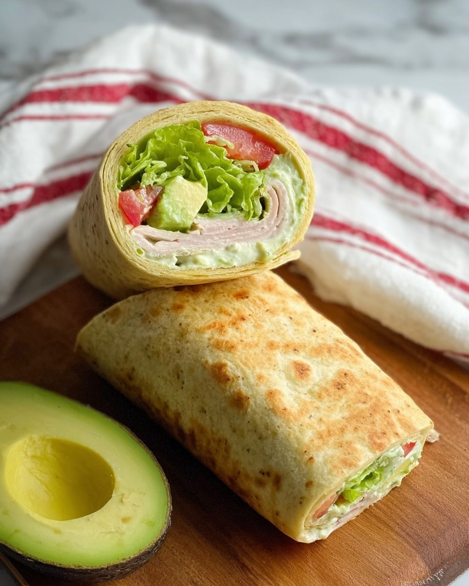 The image shows a sliced wrap sandwich resting on a wooden surface with a half avocado placed nearby. The wrap has two main layers: the outer layer is a golden-brown flatbread with a slightly crispy texture, while the inside has fresh green lettuce, red tomato pieces, pale green avocado slices, and creamy white dressing all tightly rolled together. One piece of the wrap is standing upright, showing the visible colorful filling inside, and the other piece is lying flat on the surface. In the background, there is a white towel with red stripes. The overall scene is set on a white marbled texture. photo taken with an iphone --ar 4:5 --v 7