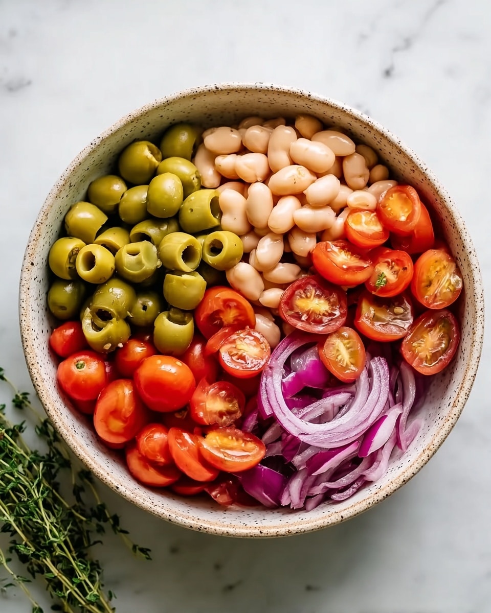 A round bowl filled with five distinct layers arranged side by side: bright green sliced olives on the top left, beige beans in the center, red cherry tomatoes cut in half on the top right, whole red cherry tomatoes on the bottom left, and thin slices of purple onion on the bottom right. The bowl is placed on a white marbled texture, with a small bunch of green herbs nearby. The overall composition is colorful and fresh. photo taken with an iphone --ar 4:5 --v 7
